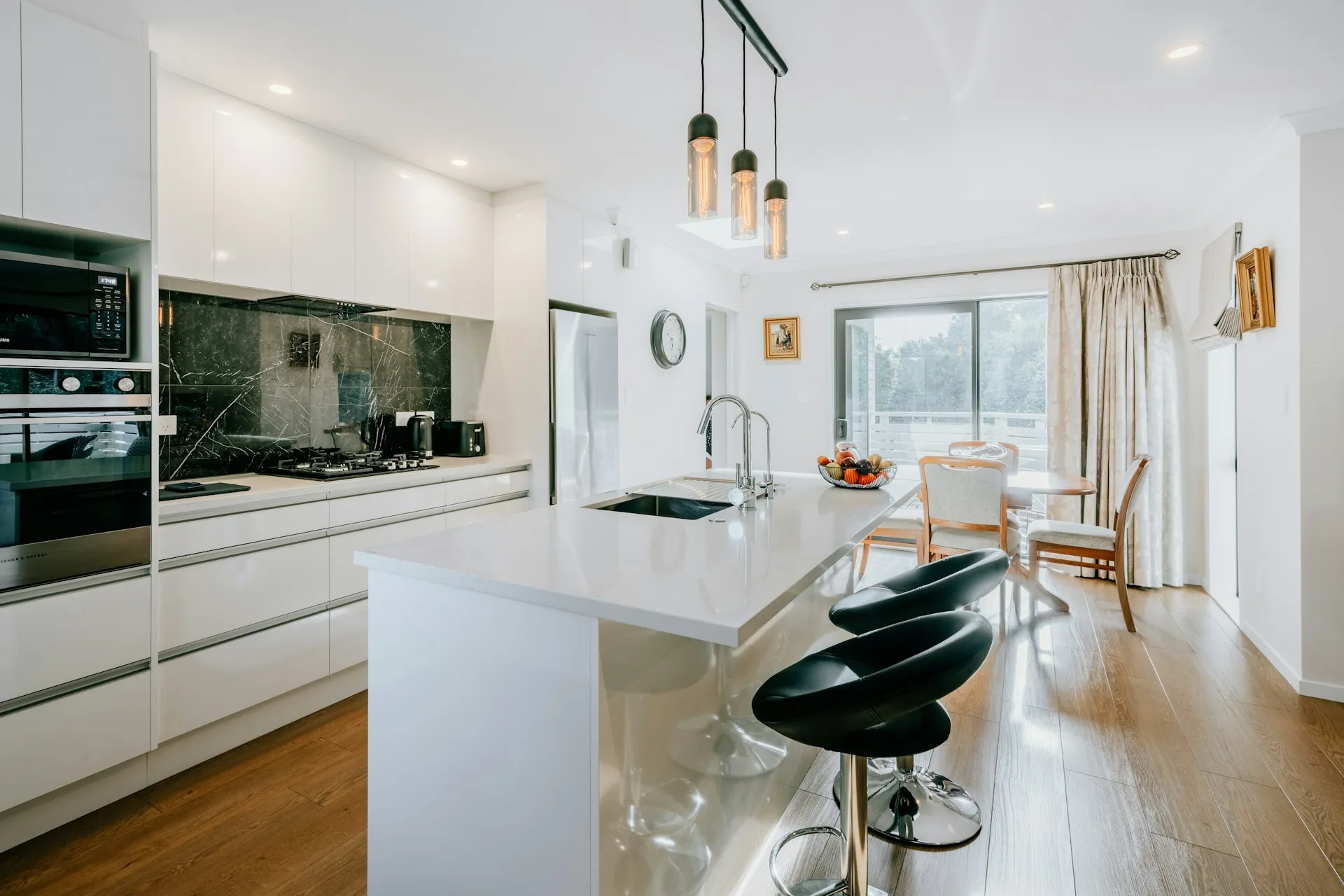 Kitchen with white cabinets, a black counter, metal appliances, and a table with chairs in the back.