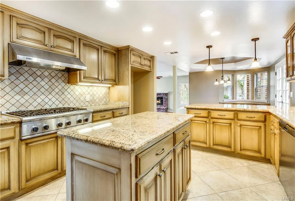 Large kitchen with wood cabinets, island, granite counter, steel appliances, tile floor, and windows
