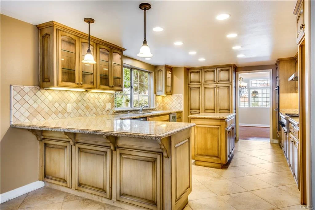 Large kitchen with wood cabinets, island, granite counter, steel appliances, tile floor, and windows
