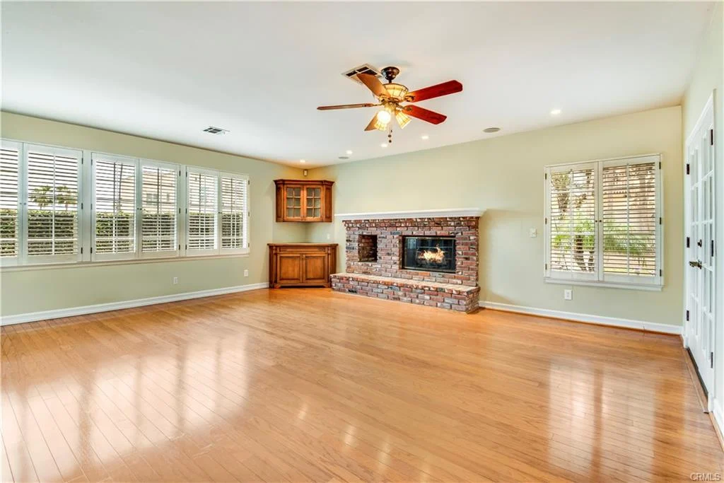 Large living room with hardwood floor, stone fireplace, ceiling fan, windows, and cabinets