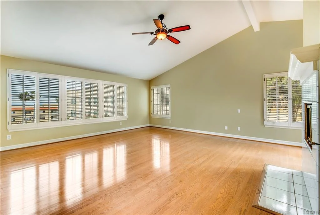 Large living room with wooden floor, ceiling fan, windows, and fireplace