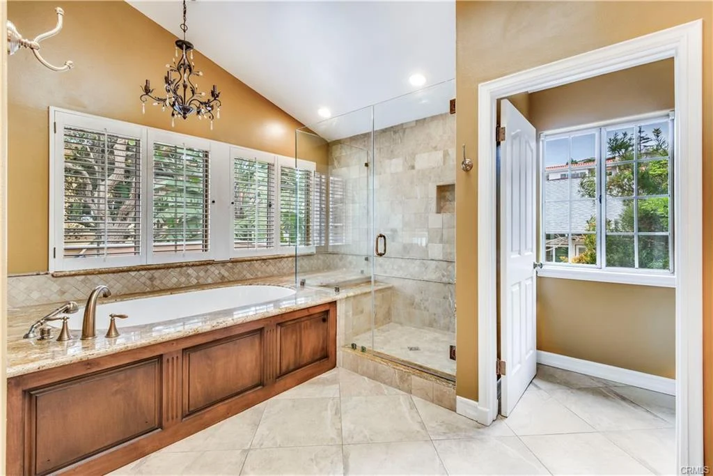 Luxury bathroom with soaking tub, glass shower, lights, warm walls, and windows