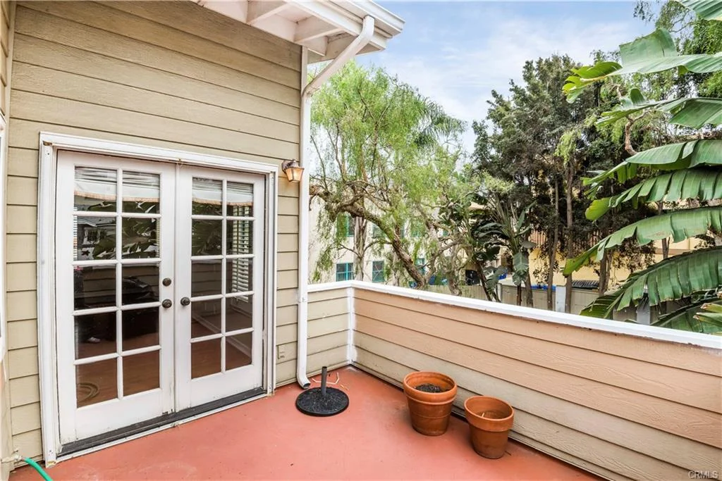 Balcony with double doors, potted plants, and greenery near a house California real estate
