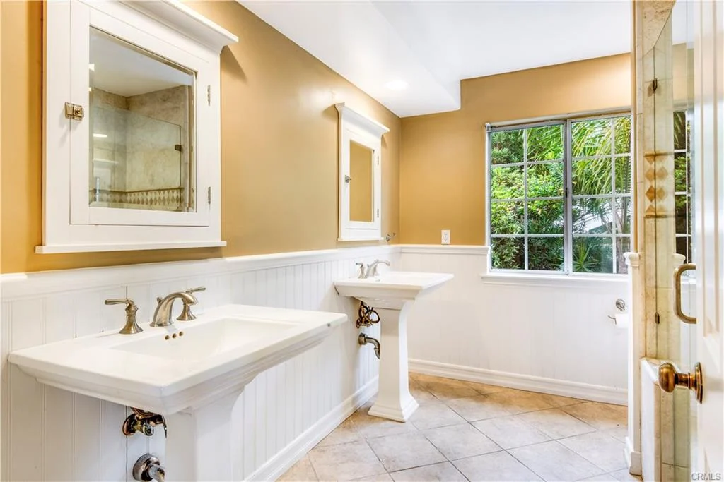 Bathroom with two sinks, big mirror, window with plants view, and beige and white walls