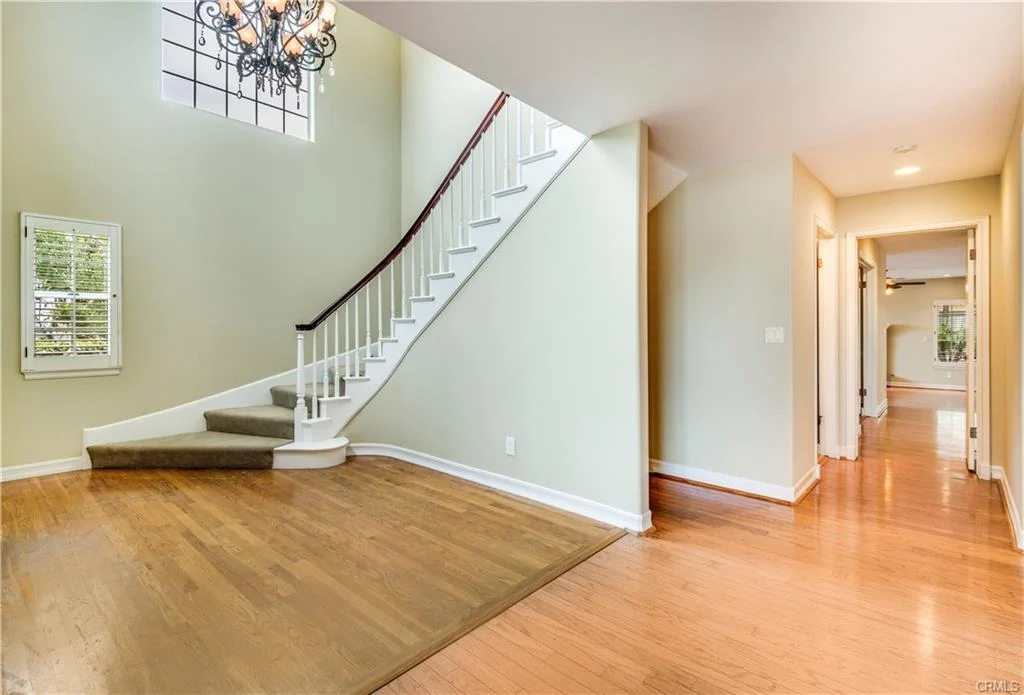 Hallway with a curved staircase, white railings, and a chandelier.