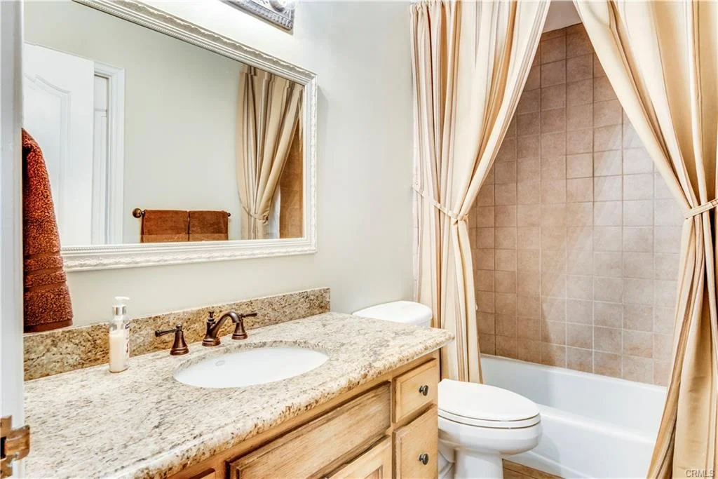 Bathroom with beige and white colors, granite counter, mirror, bathtub with curtain, and two sinks