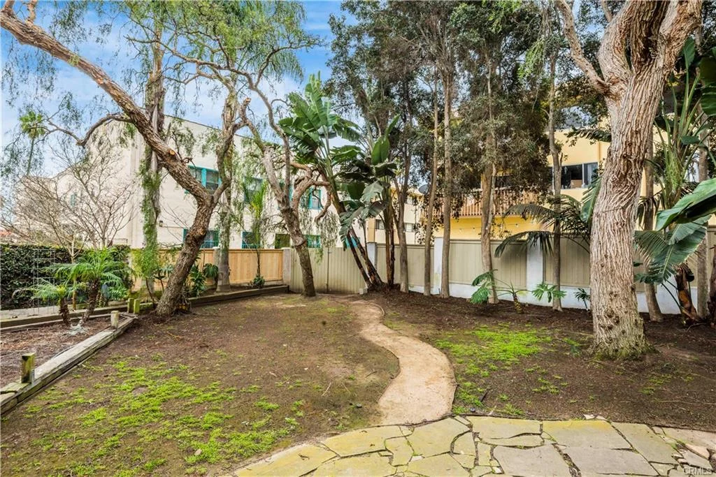 Pathway in garden with trees, shrubs, fence, and buildings near a house California real estate