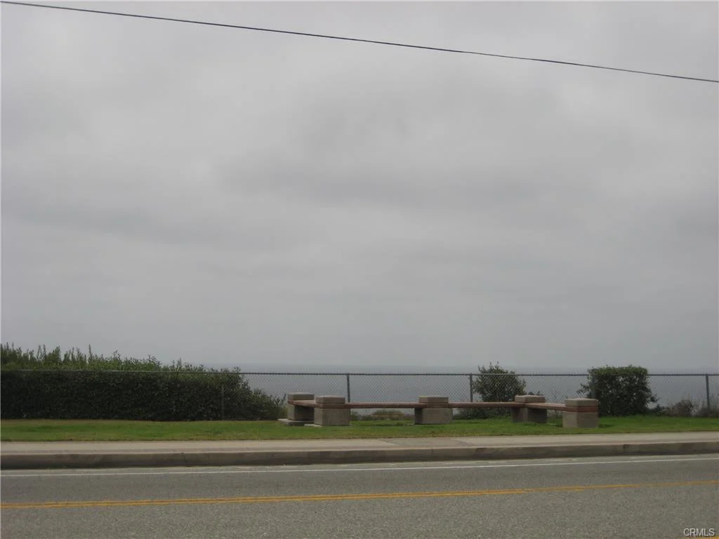 Ocean view with road, grass, and benches