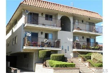 Building with balconies, tile roof, and green plants around entrance.