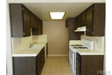 Kitchen with dark wood cabinets, white counter, sink, gas stove, light walls, and ceiling light.