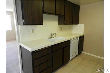 Kitchen with brown cabinets, white counter, sink, dishwasher, and light beige wall.
