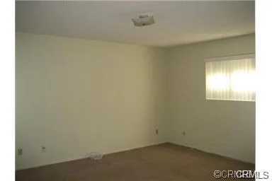 Empty room with beige carpet, plain walls, and window with curtains.