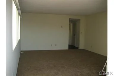 Empty room with light walls, carpet floor, windows, and door to another area.