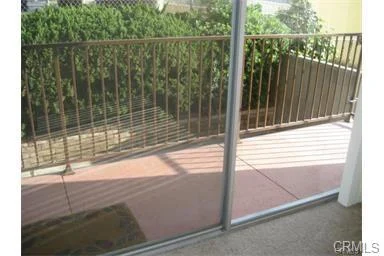 Patio view with glass sliding door, railing, and green plants outside.