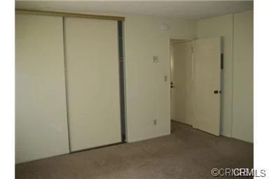 Room with beige walls, carpet floor, closet with sliding doors, and open door to another space.
