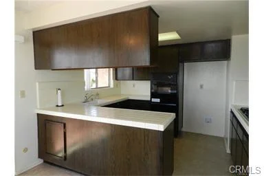 Kitchen with dark wood cabinets, white counter, and steel appliances.