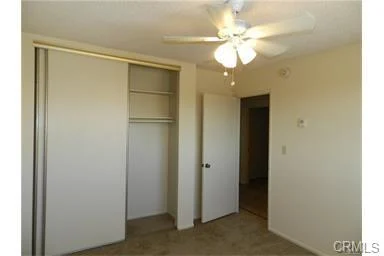 Simple bedroom with ceiling fan, closet, door, light walls, and carpet floor.
