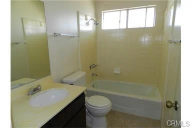 Bathroom with bathtub, toilet, sink, mirrors, and window.