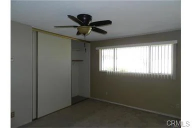 Empty room with ceiling fan, beige walls, window blinds, and closet on left side.