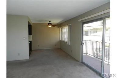 Living room with ceiling fan, large windows, sliding glass doors to balcony, carpet floor, and neutral walls.