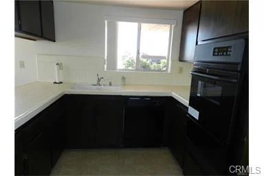 Kitchen with dark cabinets, sink under window, and oven.