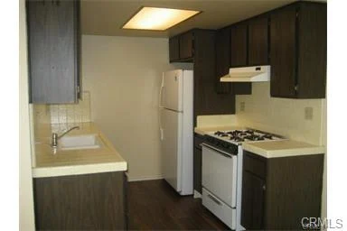Kitchen with fridge, stove, sink, dark cabinets, and light counters.