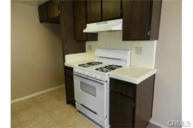 Kitchen with white gas stove, white counter, and dark wood cabinets.
