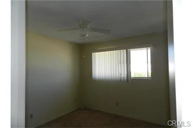 Empty room with light walls, ceiling fan, and window with blinds.