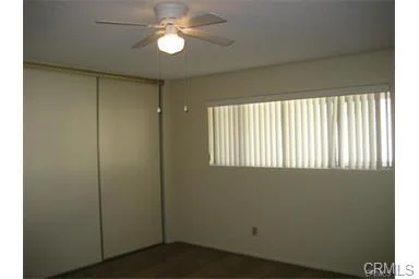 Room with ceiling fan, light, blinds on window, sliding closet doors, light walls, and carpet floor.