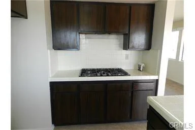 Kitchen with dark wood cabinets, white counter, and stove in center.