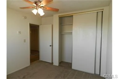 Room with ceiling fan, light fixture, sliding closet doors, and door to another space.