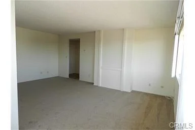 Empty room with white walls, light floor, large windows, and doorway to another area.