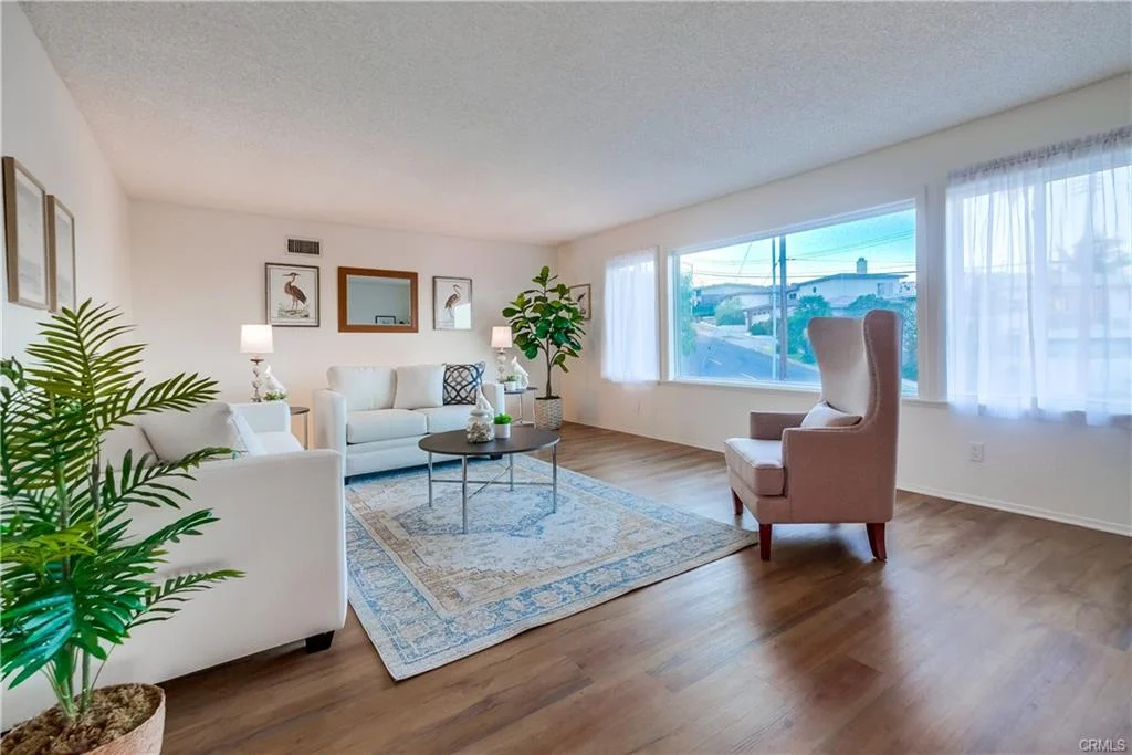 Living room with white sofa, small table, window, plants, wall pictures, and chair