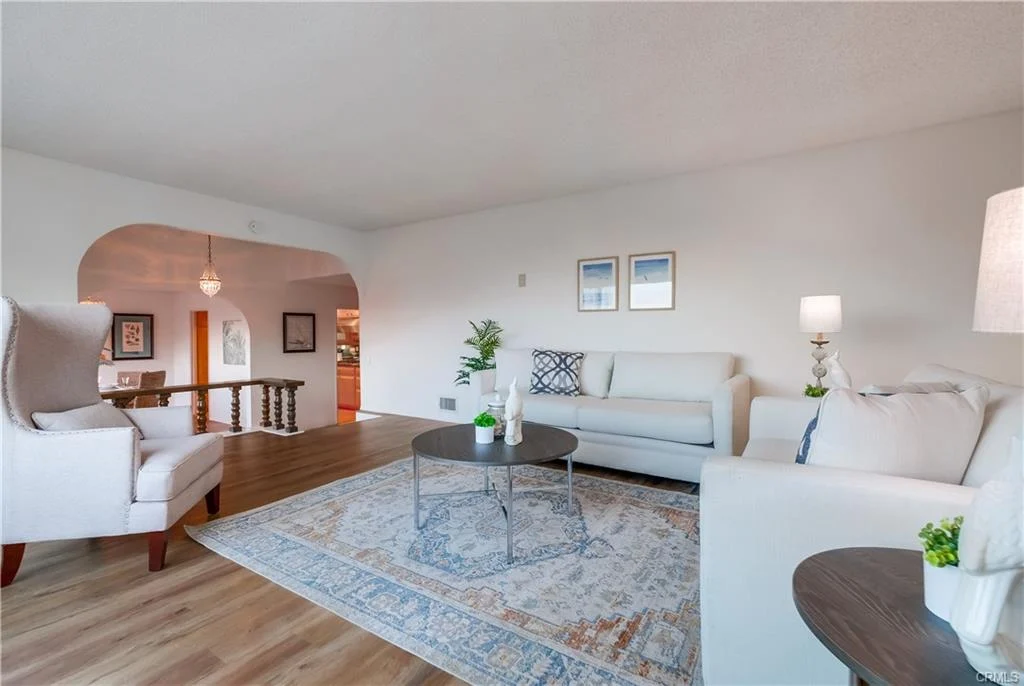 Living room with white sofas, coffee table, rug, plants, and wall pictures