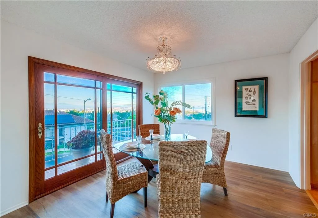Dining area with glass table, wicker chairs, chandelier, flowers, and wall art inside a home