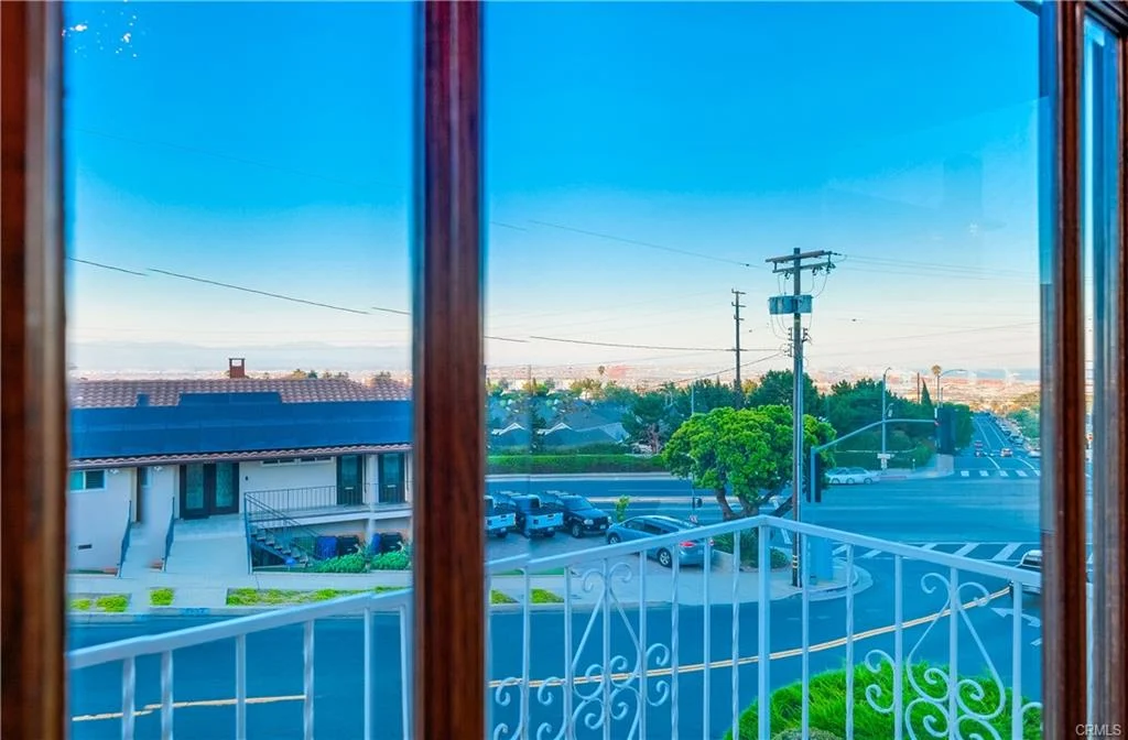 Window view of houses in a neighborhood with sky, power lines, and hills in California real estate near house