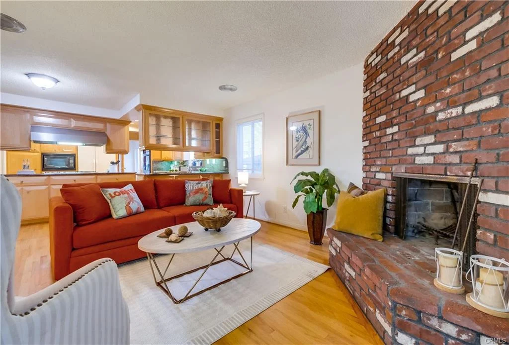 Living room with red sofa, coffee table, brick fireplace, plants, pillows, and windows.