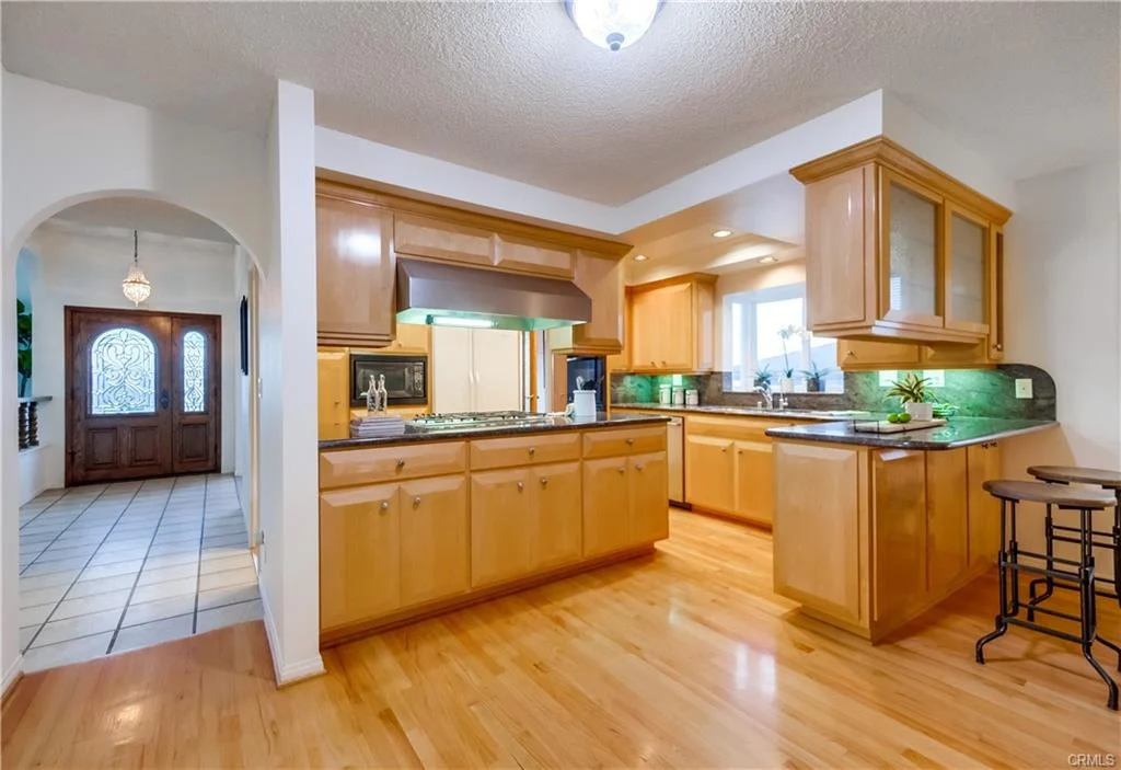 Kitchen with wooden cabinets, hardwood floor, bar stool, hallway entrance, appliances, and window.
