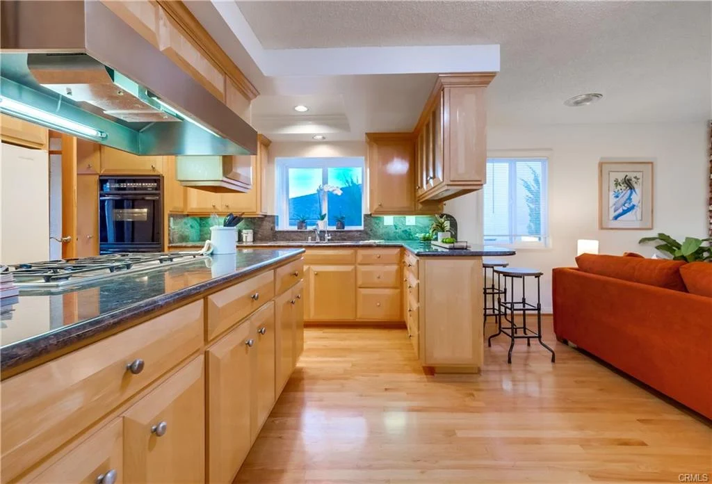 Kitchen with wooden cabinets, granite countertops, stove, and view to living area with orange couch.