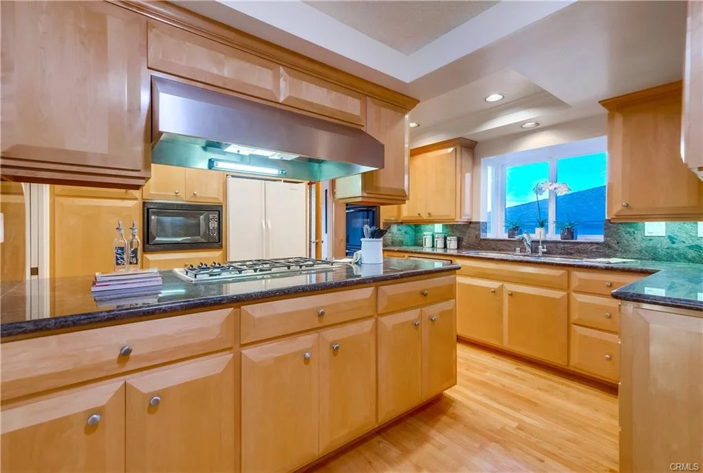 Kitchen with wooden cabinets, gas stove island, granite countertops, appliances, and windows.