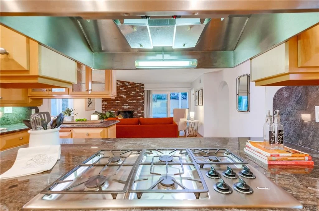 Kitchen with gas stovetop and view to living area with red sofa and windows.
