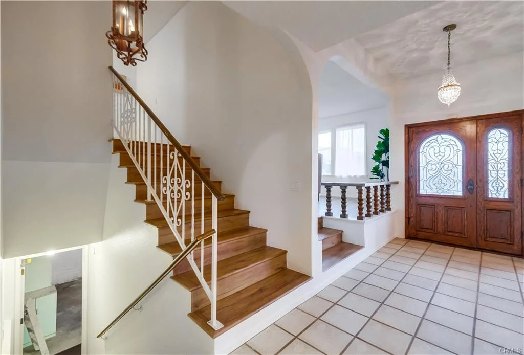 Staircase with wooden steps, white railings, foyer, double doors, and light fixture.
