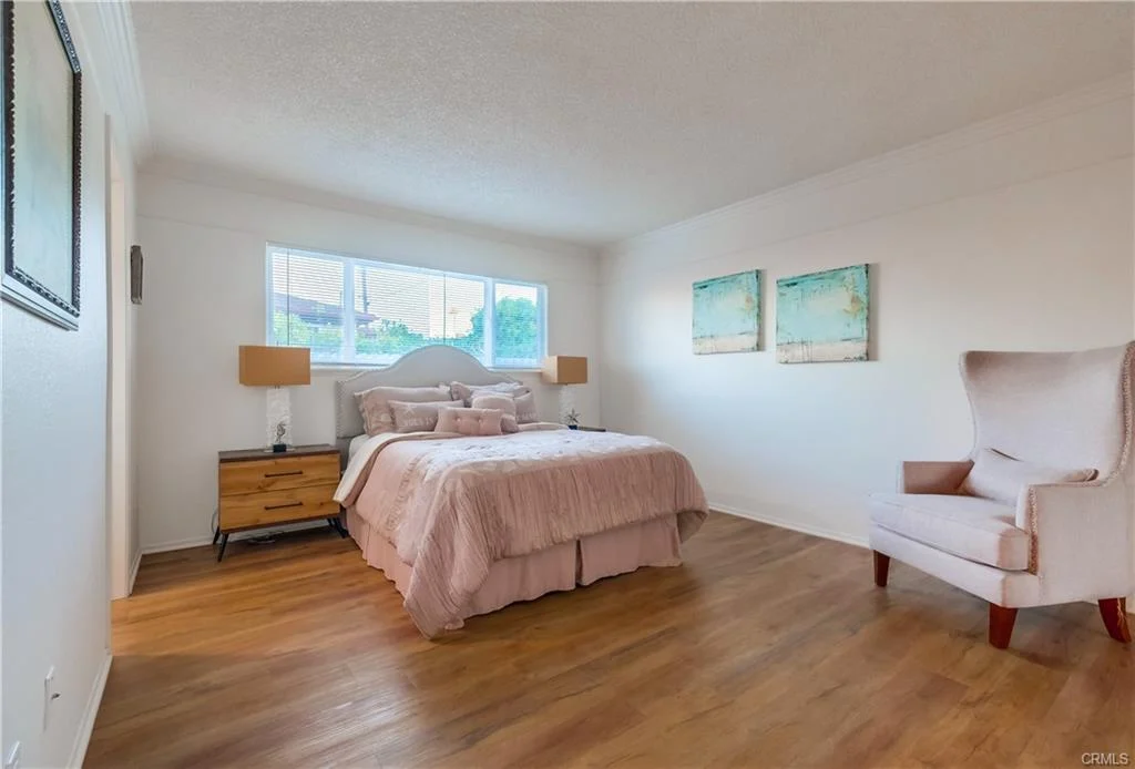 Bedroom with bed, pink bedding, bedside lamps, window, and chair.