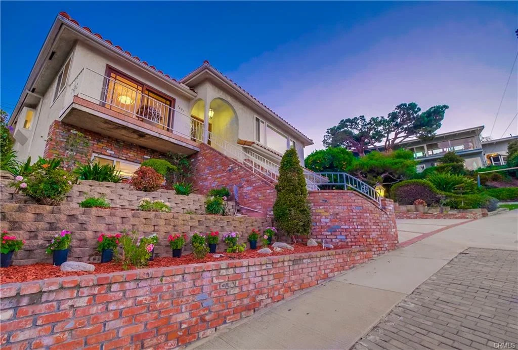 Luxury house in California real estate with brick pathway, balcony, flowers, and greenery