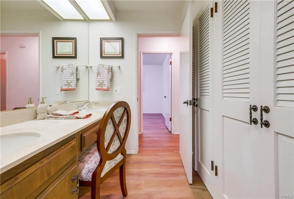 Bathroom with vanity, sink, wooden cabinets, chair, towels, wooden floor, and framed pictures.