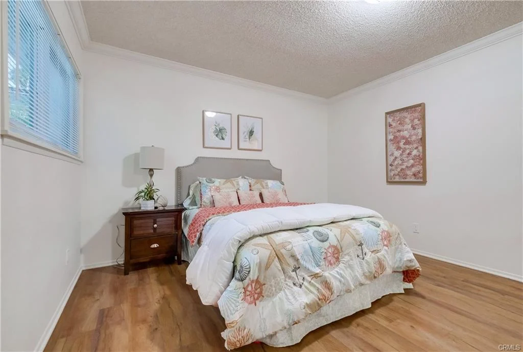 Bedroom with bed, floral bedding, side table with lamp, wall art, and wood floor.
