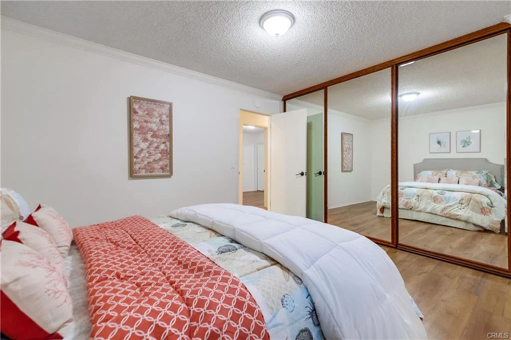 Bedroom with bed, patterned comforter, pillows, mirror wardrobe, framed artwork, and wood floor.