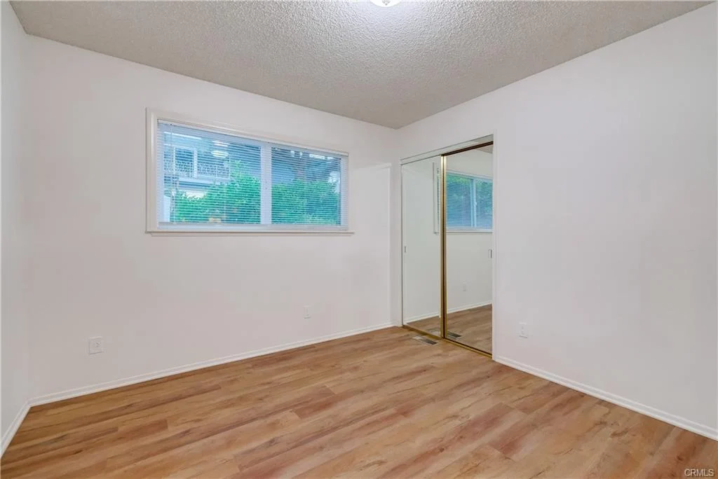 Room with light walls, window, mirrored closet door, and wood floor.