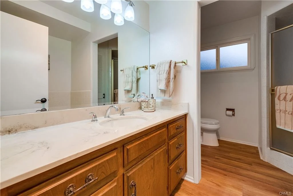 Bathroom with double sink vanity, wooden cabinets, large mirror, neutral walls, towels, toilet, and shower.