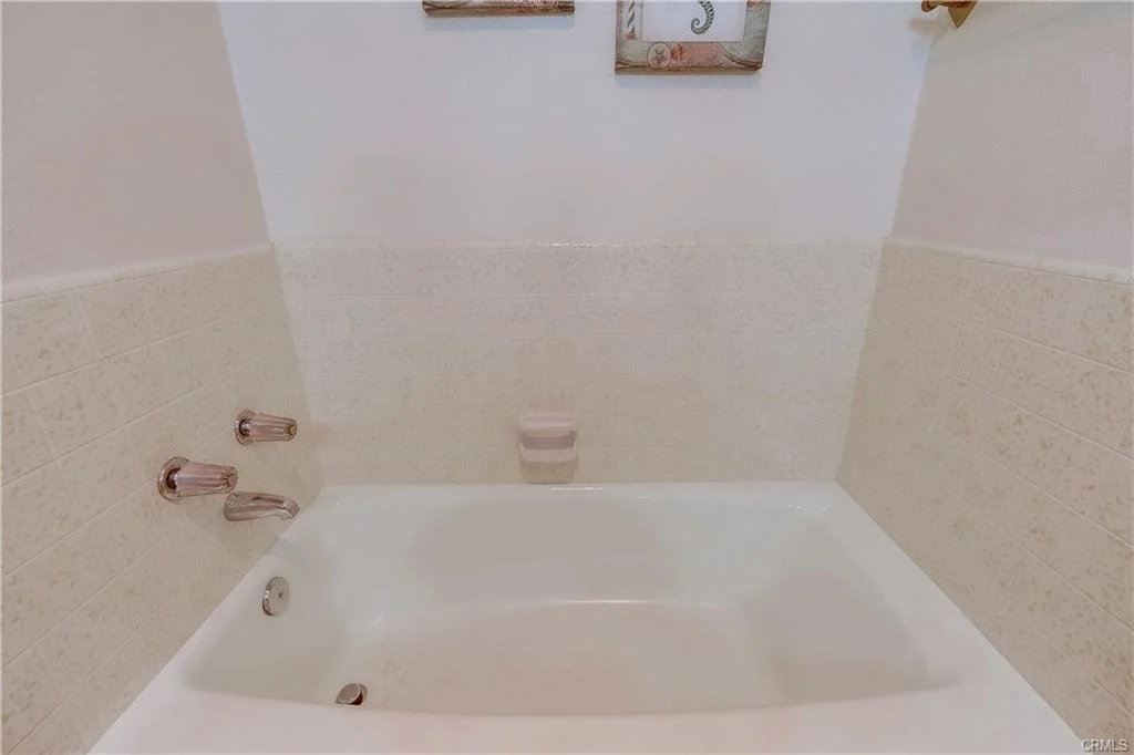 Bathtub with chrome fixtures and light-colored tiled wall.